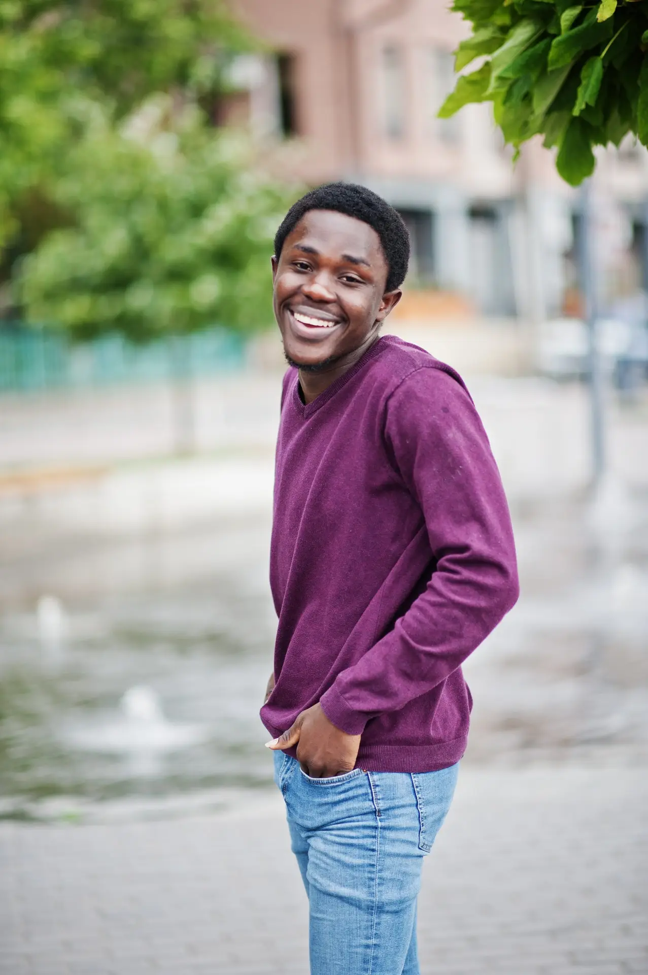 Young african american man in violet jumper posed against fountain alley.
